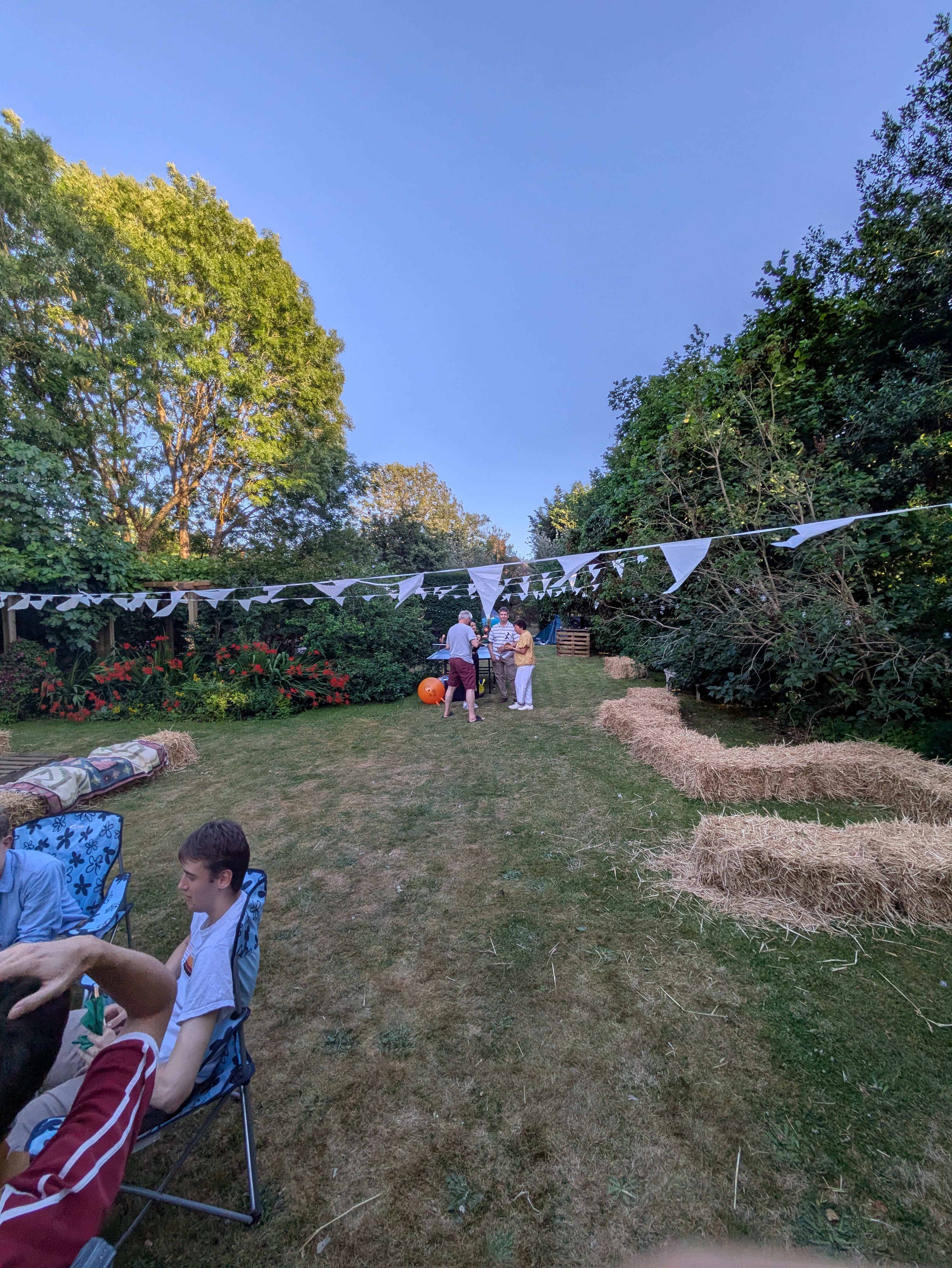 A picture of a sunny garden with hay bales to sit on and bunting hung between the trees