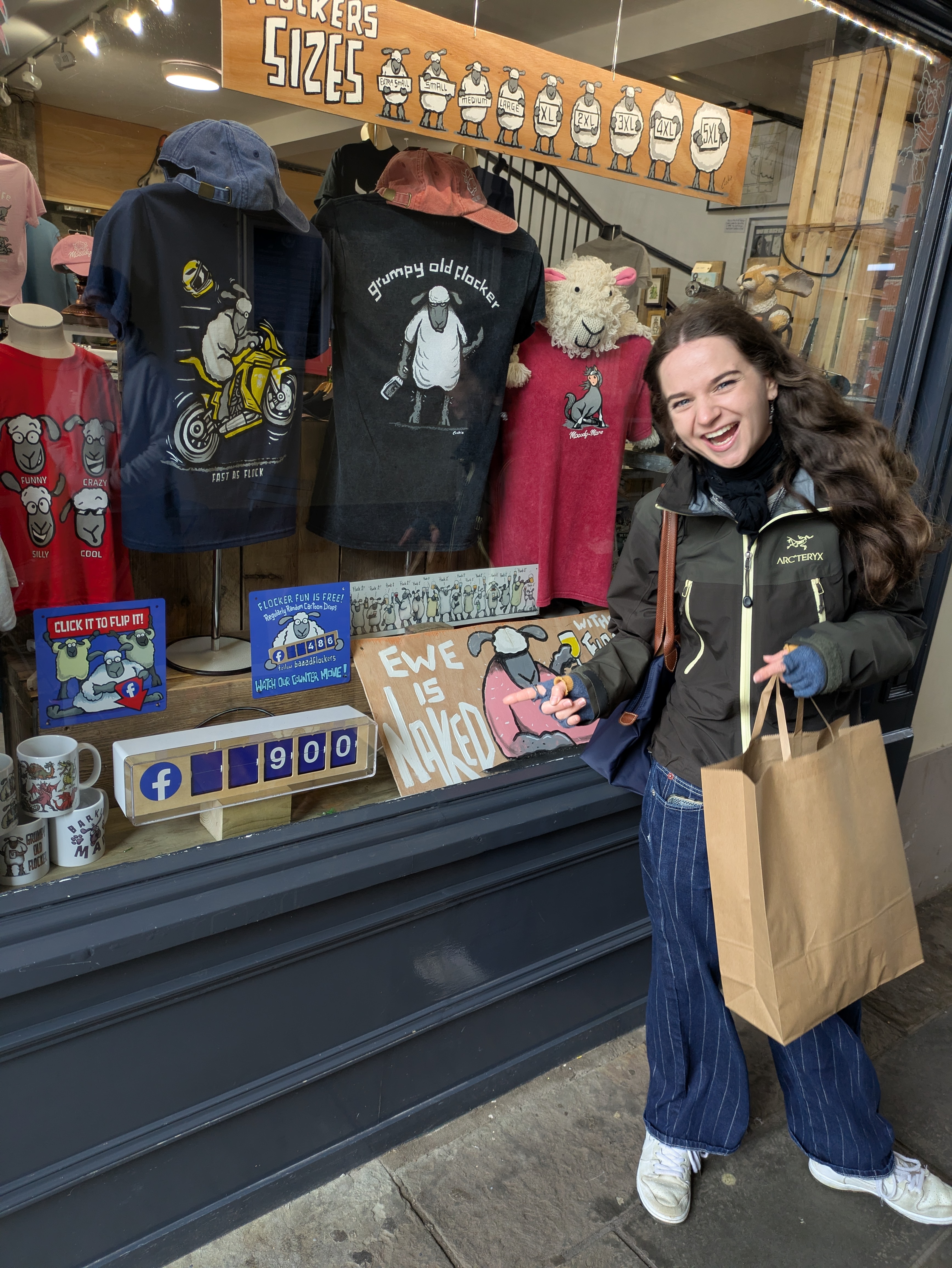 A photo of Grace in front of the Baaad Flockers shop window, pointing to a Facebook follower counter reading 900